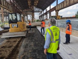 esperto di radioprotezione con casacca gialla che sorveglia il posto di lavoro. Nello sfondo altri due operai che lavorano